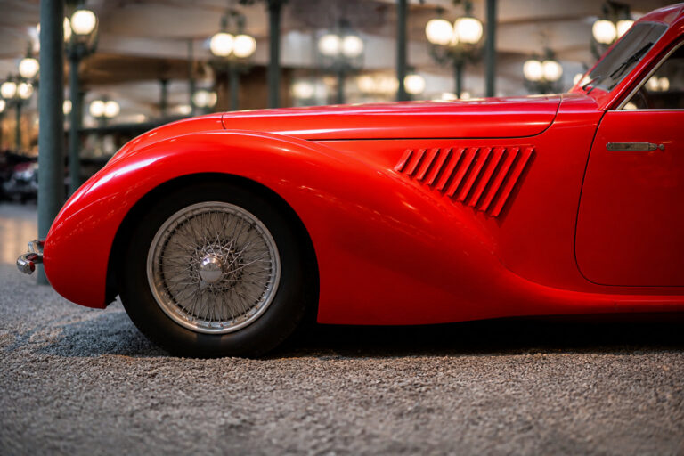 Gros plan sur l'aile avant et la roue à rayons d'une voiture de collection rouge vif dans un musée.