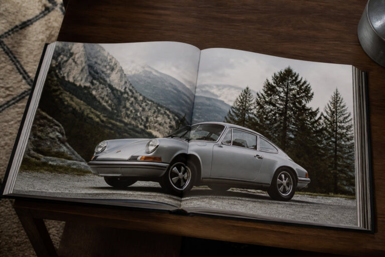 Un livre ouvert sur une table montrant la photo d'une Porsche 911 classique garée dans un paysage de montagne.