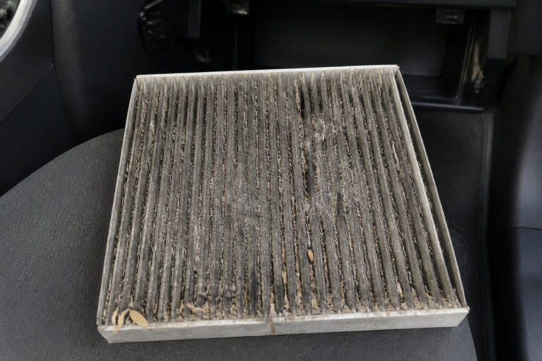Un filtre d'habitacle de voiture usagé et très encrassé posé sur un siège de véhicule.