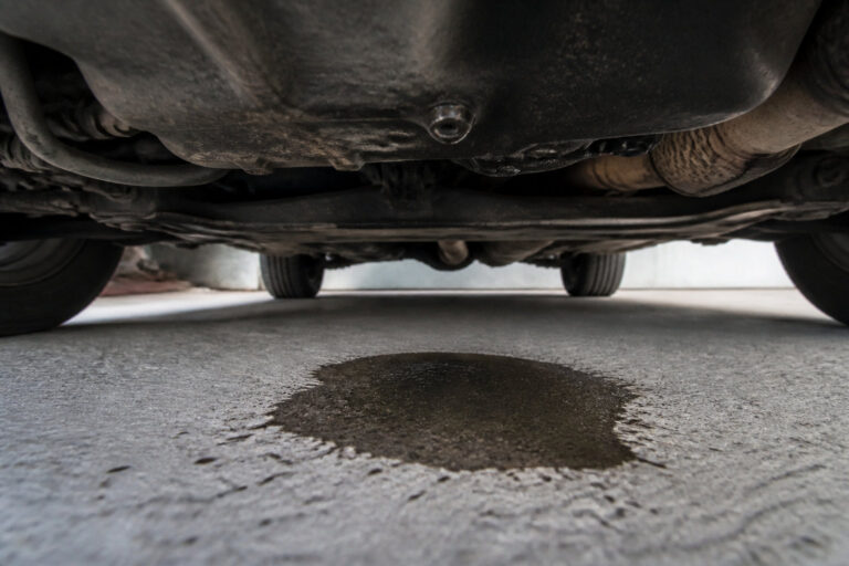 Une flaque de liquide sous le châssis d'une voiture garée sur du béton.