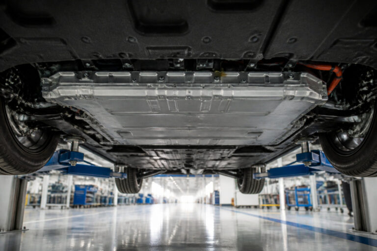 Vue en contre-plongée du soubassement d'une voiture électrique levée sur un pont dans un atelier de réparation.