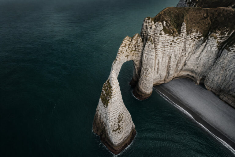 Vue aérienne des falaises blanches d'Étretat plongeant dans la mer sombre.