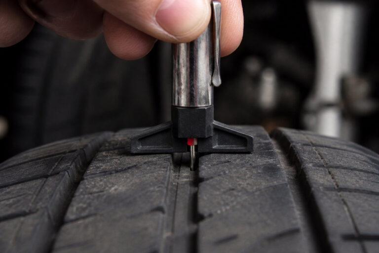 Main utilisant une jauge de profondeur pour mesurer l'usure des sculptures d'un pneu de voiture.