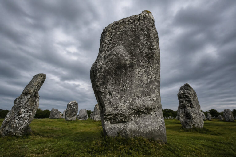 Gros plan sur les imposants menhirs des alignements de Carnac en Bretagne sous un ciel nuageux.