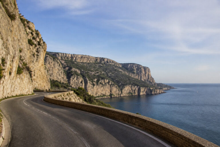 Une route sinueuse longe des falaises escarpées surplombant la mer Méditerranée sous un ciel bleu dégagé.
