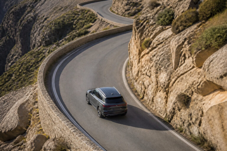 Vue aérienne d'un SUV gris parcourant une route de montagne sinueuse avec des falaises rocheuses.