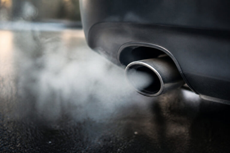 Gros plan sur un pot d'échappement de voiture libérant de la vapeur blanche sur une route humide par temps froid.