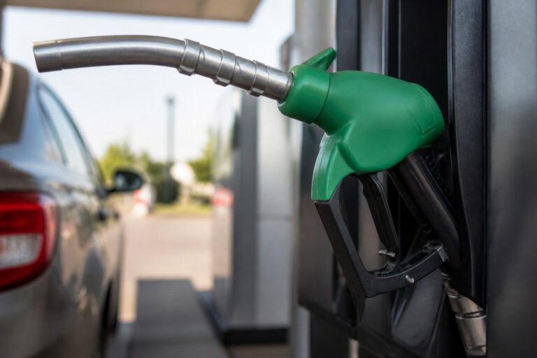 Pistolet de pompe à essence vert sur le côté d'une station-service avec une voiture en arrière-plan.