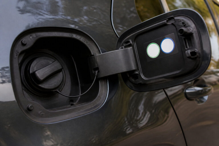 Trappe à carburant ouverte d'une voiture grise avec bouchon noir et autocollants de signalétique sur la face intérieure.